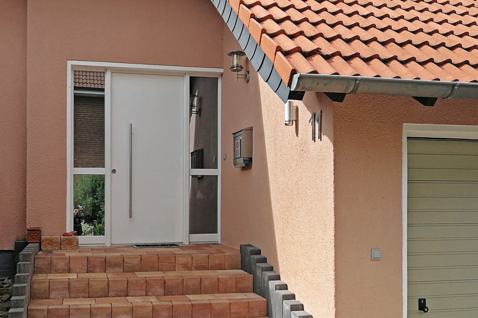 Eingang eines pfirsichfarbenen Hauses mit weißer Tür, Backsteinstufen und Ziegeldach
